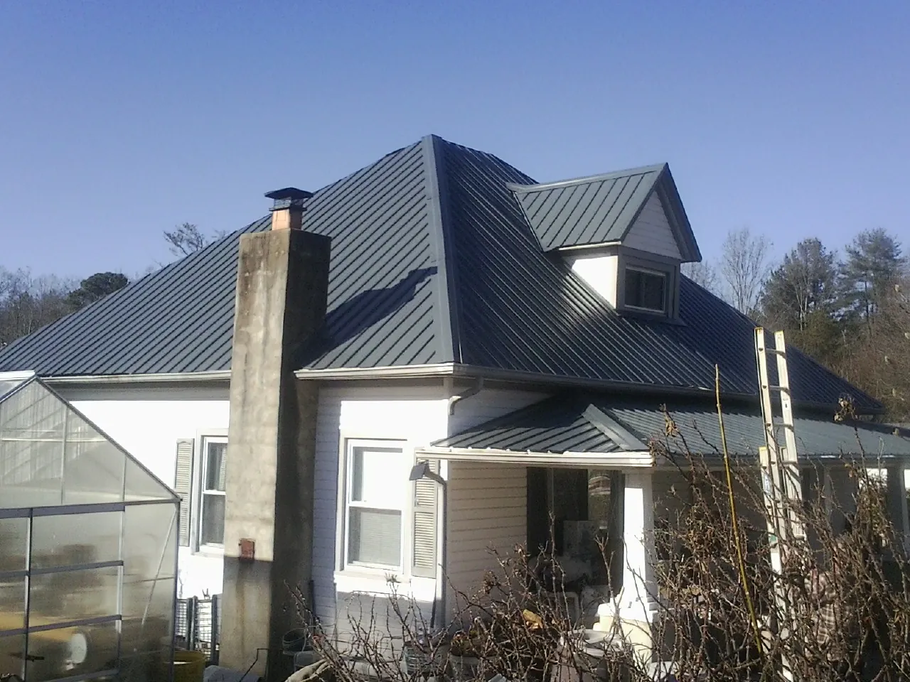 Dark blue standing seam metal roof on a white farmhouse with dormer — Slate & Tile Roof Repair by Roofing Brothers in West Brookfield