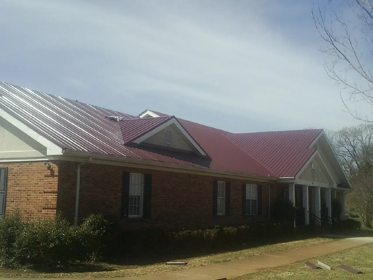 Red metal roof with gabled entries on a long brick building, from a Hail Damage Roof Repair job in West Brookfield