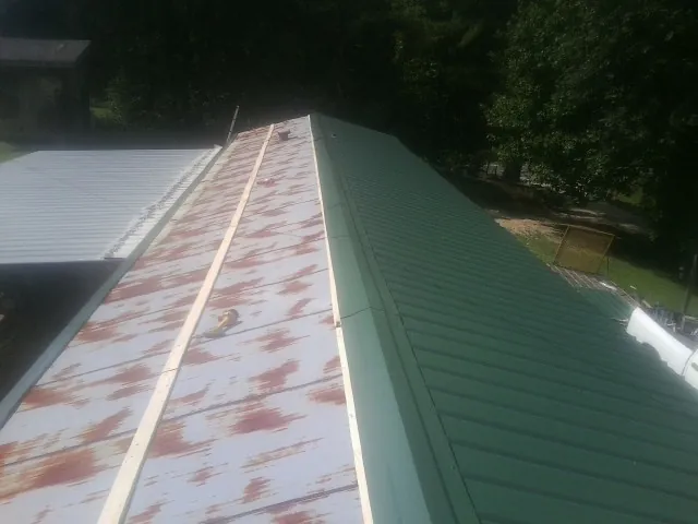 Old rusted panels beside newly installed green metal roofing — Wind Damage Roof Repair by Roofing Brothers in West Brookfield