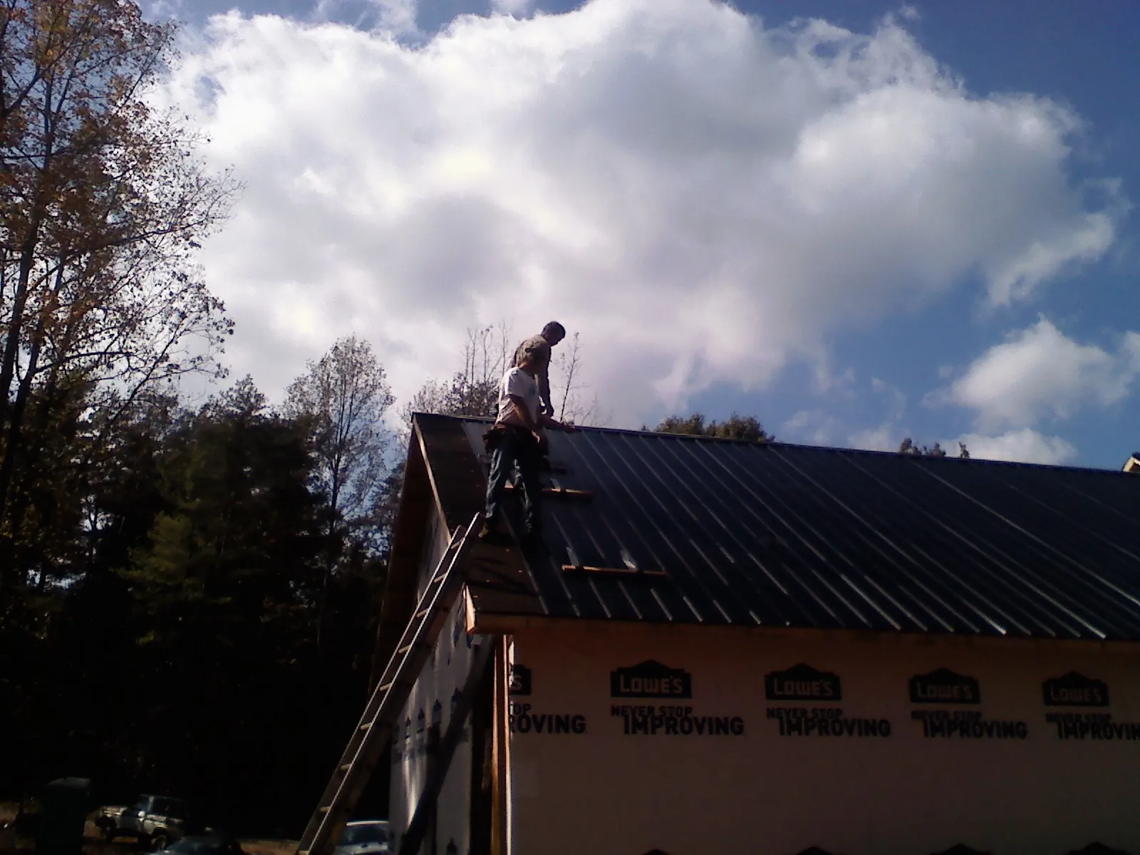 Roofer fastening dark metal panels high against a cloudy sky, from a Roof Inspection job in West Brookfield