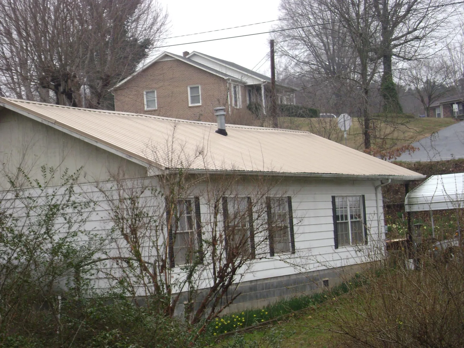 Tan metal roof on a white sided house set into a hillside — Commercial Roofing by Roofing Brothers in West Brookfield