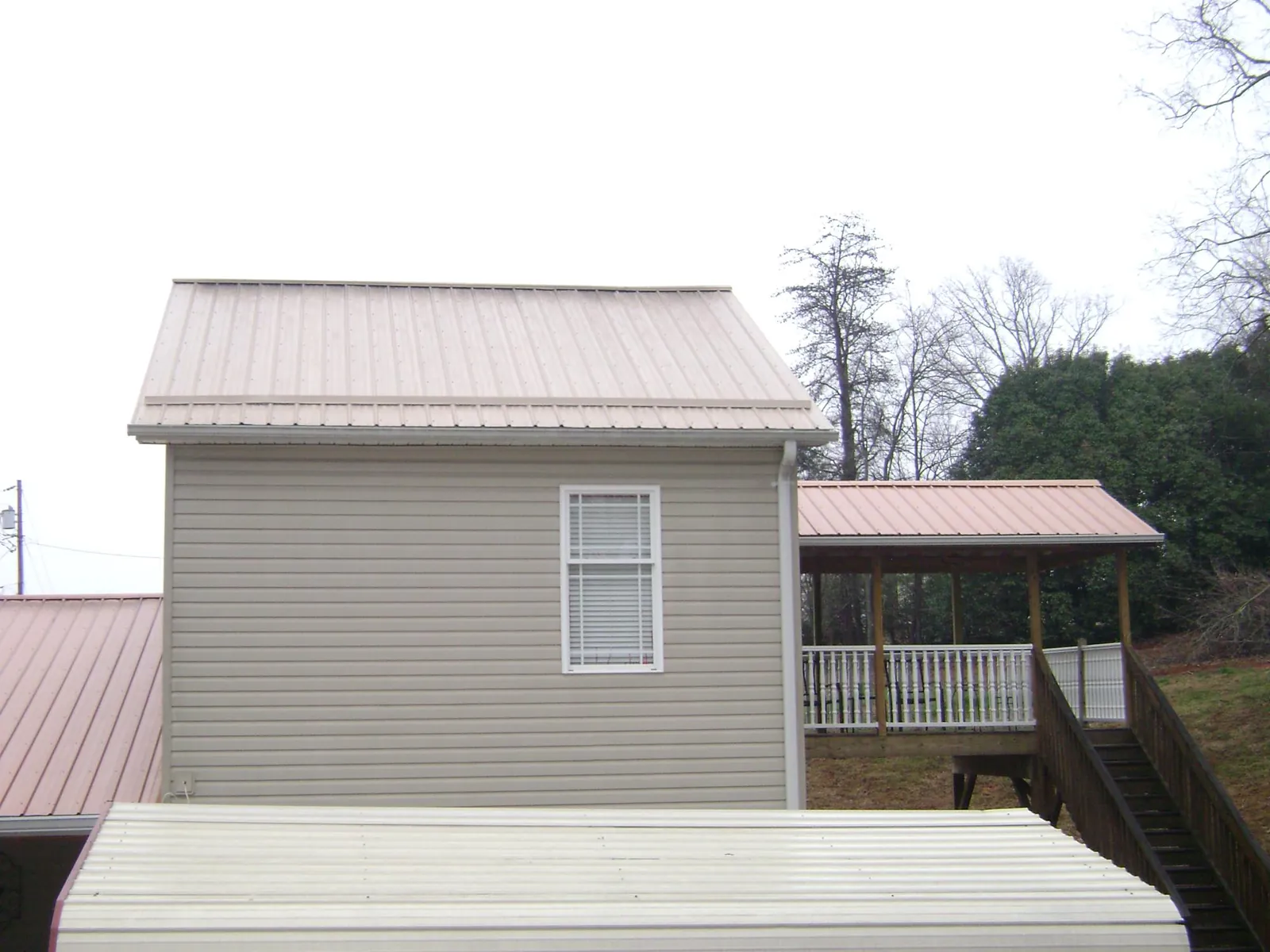 Tan metal roofs on a two story addition and attached porch, from a Roof Replacement job in West Brookfield